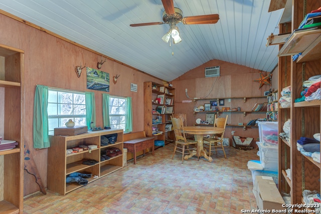 home office with ceiling fan, wood walls, and vaulted ceiling