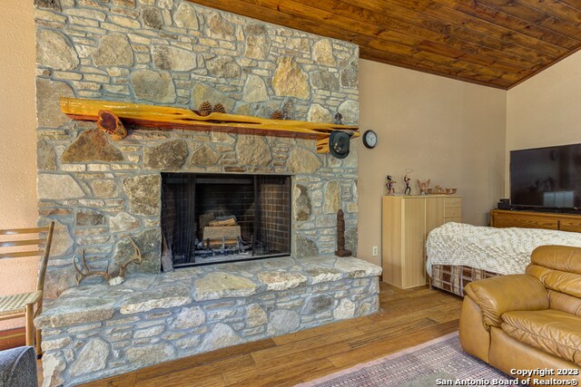 living room featuring wood ceiling, lofted ceiling, a stone fireplace, and dark hardwood / wood-style floors