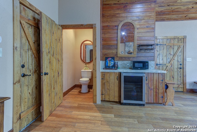 kitchen featuring wine cooler, wood walls, backsplash, and light hardwood / wood-style floors