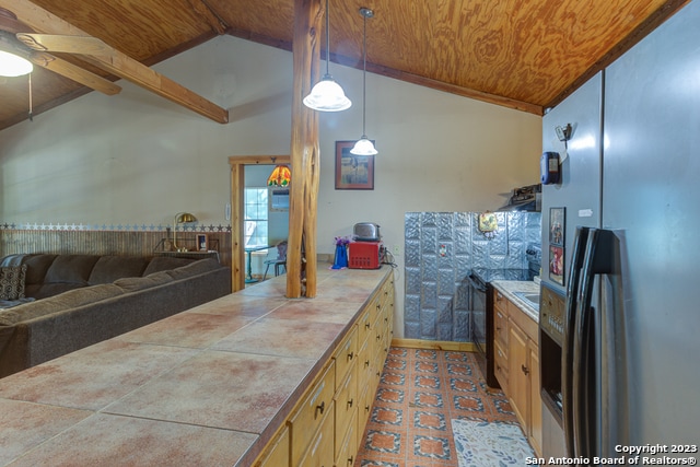 kitchen featuring decorative light fixtures, beam ceiling, ceiling fan, tile counters, and stainless steel refrigerator with ice dispenser