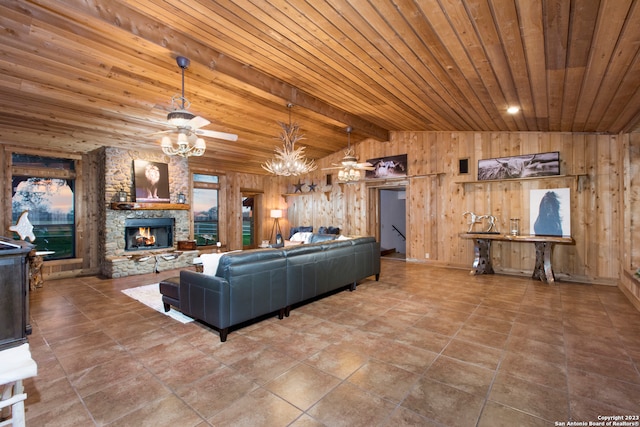 living room featuring wooden walls, tile floors, wooden ceiling, ceiling fan with notable chandelier, and a stone fireplace