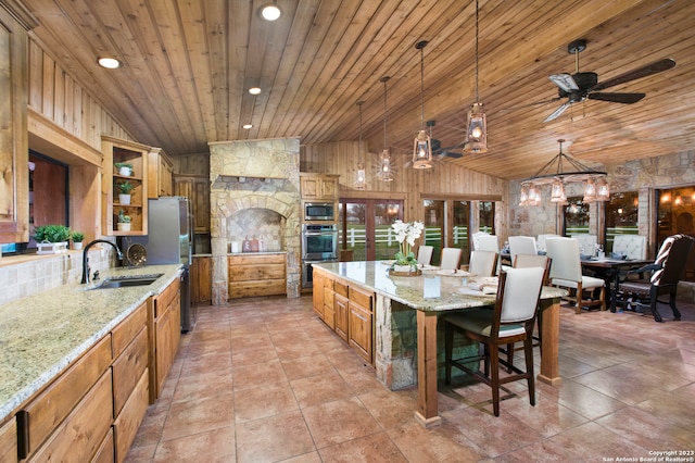 kitchen featuring sink, wood ceiling, stainless steel appliances, light stone countertops, and a kitchen bar