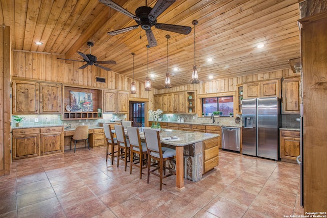 kitchen featuring pendant lighting, ceiling fan, appliances with stainless steel finishes, light stone countertops, and a center island