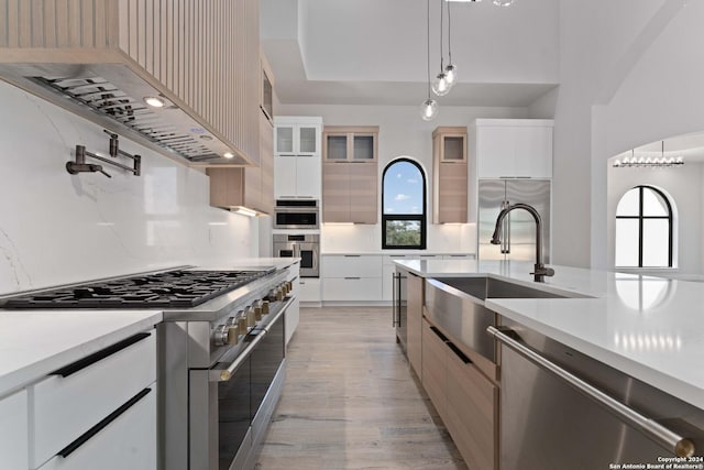 kitchen featuring pendant lighting, tasteful backsplash, white cabinets, premium appliances, and wall chimney range hood