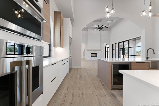 kitchen featuring pendant lighting, white cabinets, wine cooler, stainless steel oven, and light wood-type flooring