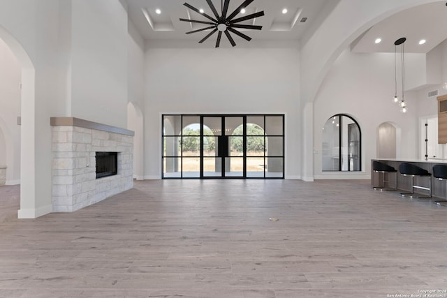 unfurnished living room featuring a towering ceiling, a fireplace, and light wood-type flooring