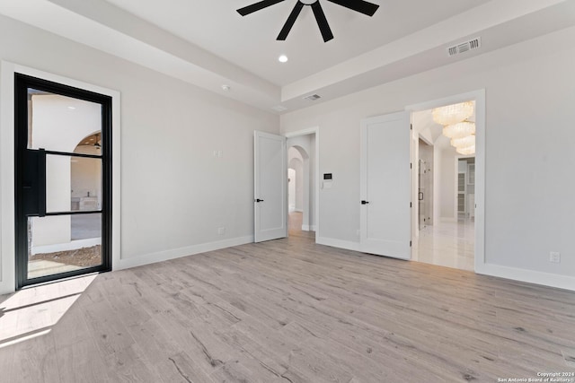 unfurnished bedroom featuring connected bathroom, a tray ceiling, ceiling fan, and light wood-type flooring