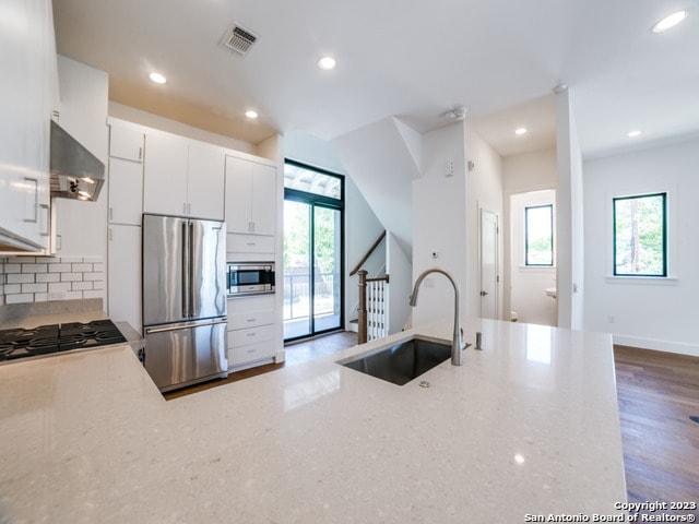 kitchen featuring hardwood / wood-style floors, stainless steel appliances, backsplash, white cabinetry, and wall chimney exhaust hood