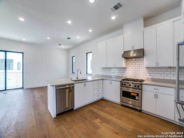 kitchen with tasteful backsplash, wood-type flooring, stainless steel appliances, sink, and white cabinetry