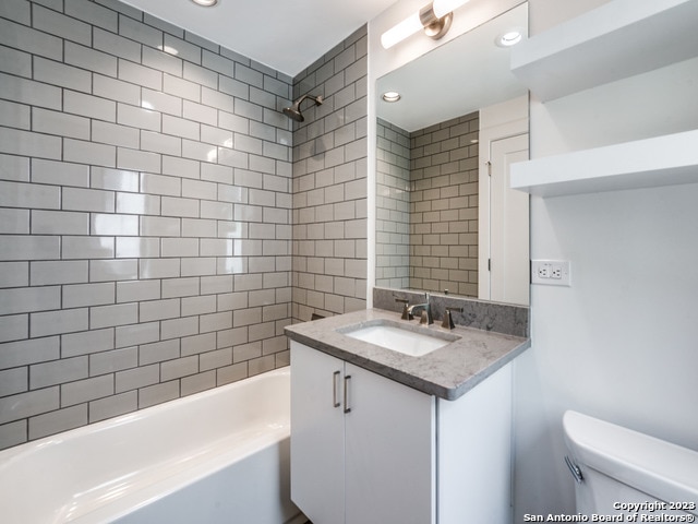 full bathroom featuring tiled shower / bath combo, toilet, and vanity