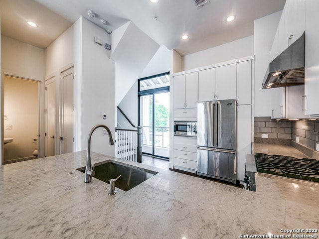 kitchen with light stone countertops, backsplash, sink, stainless steel appliances, and white cabinets