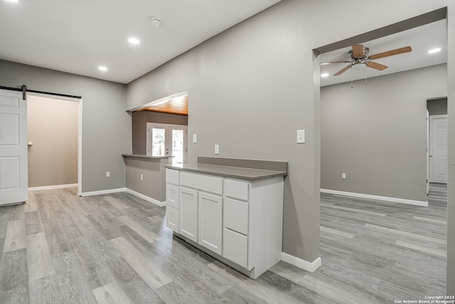 kitchen with ceiling fan, a barn door, light hardwood / wood-style floors, and white cabinets