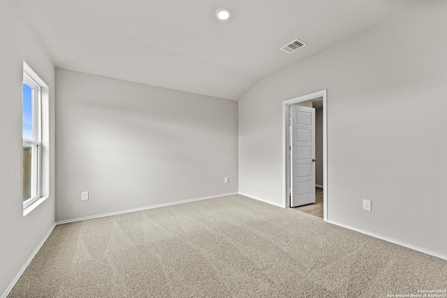 spare room with light carpet, vaulted ceiling, and plenty of natural light