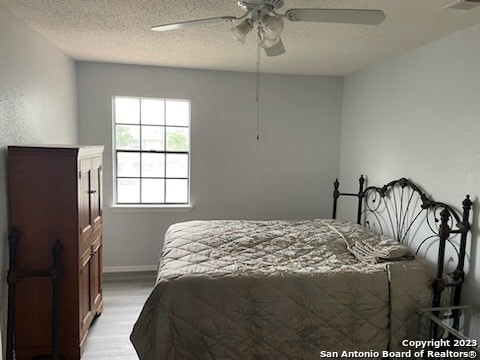 bedroom with ceiling fan, light hardwood / wood-style flooring, and a textured ceiling