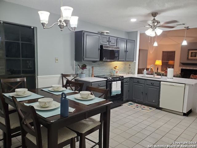 kitchen featuring decorative light fixtures, tasteful backsplash, black appliances, ceiling fan with notable chandelier, and sink