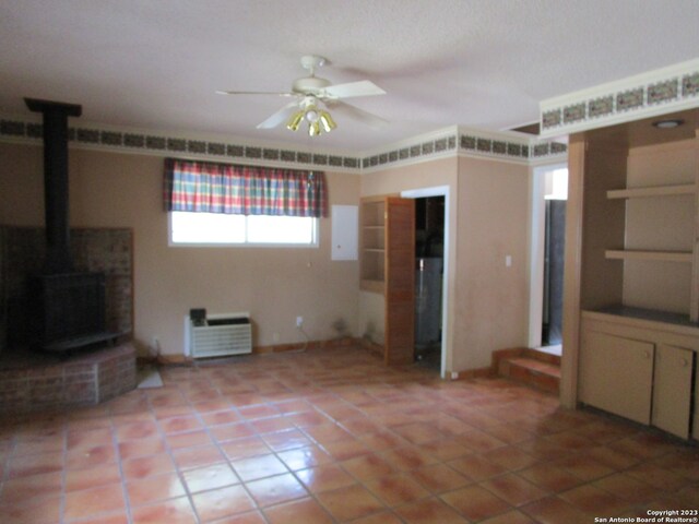 unfurnished living room featuring ceiling fan, a wood stove, and tile flooring