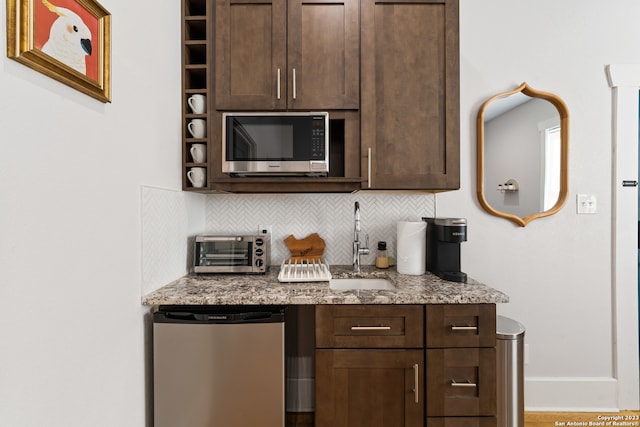 interior space featuring light stone countertops, appliances with stainless steel finishes, backsplash, dark brown cabinetry, and sink