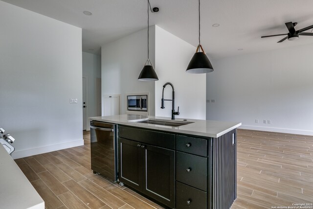 kitchen with an island with sink, sink, ceiling fan, stainless steel microwave, and hanging light fixtures