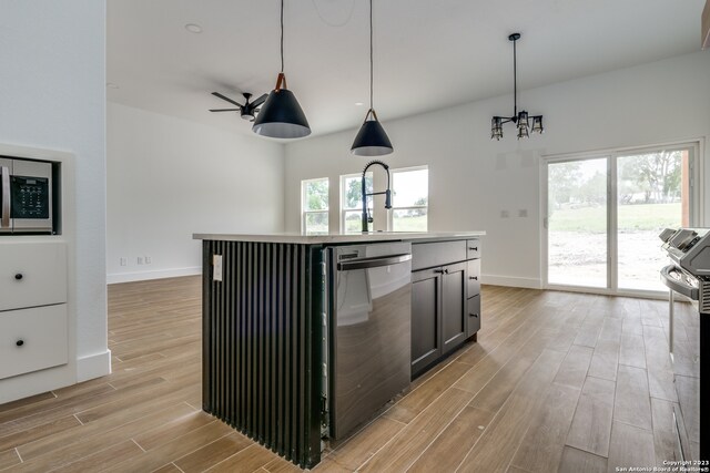 kitchen featuring decorative light fixtures, light hardwood / wood-style floors, stainless steel appliances, a kitchen island with sink, and ceiling fan with notable chandelier