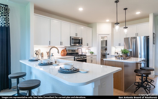 kitchen with pendant lighting, white cabinets, appliances with stainless steel finishes, light hardwood / wood-style flooring, and a kitchen bar