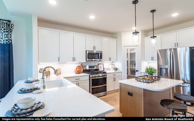 kitchen with sink, pendant lighting, white cabinets, light hardwood / wood-style flooring, and stainless steel appliances