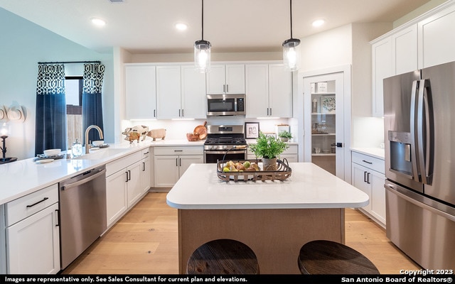 kitchen with sink, light hardwood / wood-style flooring, stainless steel appliances, decorative light fixtures, and white cabinetry