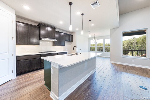 kitchen featuring an island with sink, sink, light hardwood / wood-style floors, decorative light fixtures, and dark brown cabinetry