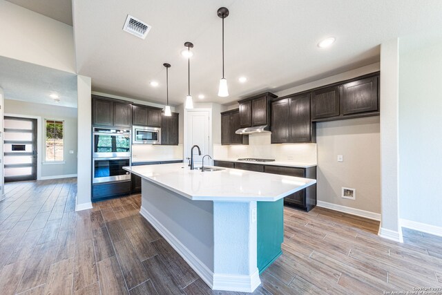 kitchen with pendant lighting, an island with sink, stainless steel appliances, sink, and dark brown cabinetry