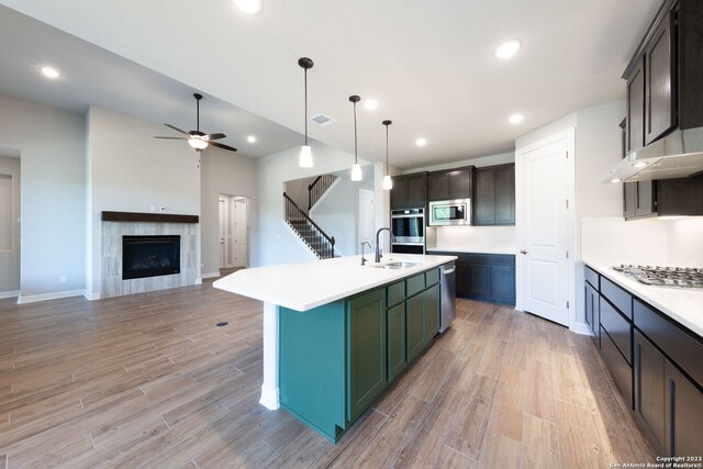 kitchen featuring decorative light fixtures, a tile fireplace, stainless steel appliances, a kitchen island with sink, and ceiling fan