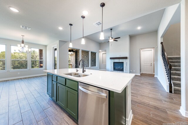 kitchen featuring an island with sink, sink, dishwasher, a tiled fireplace, and ceiling fan with notable chandelier