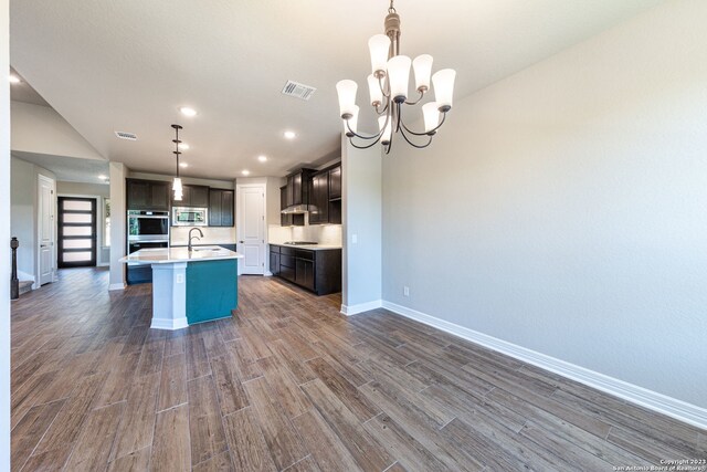 kitchen with a kitchen island with sink, sink, stainless steel appliances, decorative light fixtures, and a notable chandelier