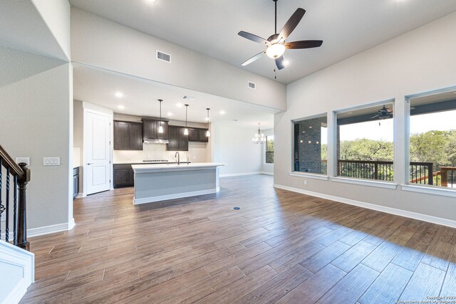 interior space featuring pendant lighting, hardwood / wood-style flooring, ceiling fan with notable chandelier, dark brown cabinets, and a kitchen island with sink