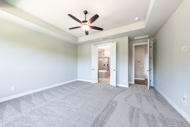 unfurnished bedroom featuring ceiling fan, ensuite bathroom, light carpet, and a tray ceiling