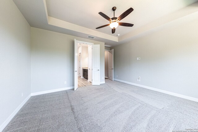 unfurnished bedroom with ceiling fan, a tray ceiling, and light carpet