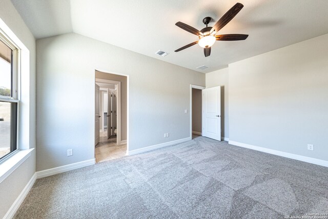 unfurnished bedroom featuring light colored carpet, ceiling fan, vaulted ceiling, and multiple windows