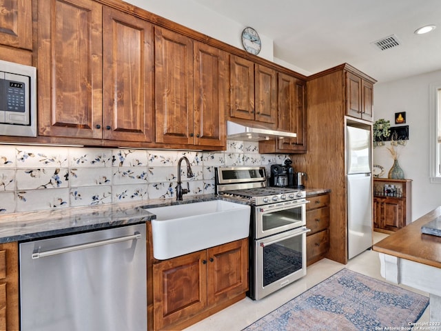 kitchen with sink, light tile floors, dark stone countertops, stainless steel appliances, and tasteful backsplash