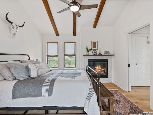 bedroom featuring a high end fireplace, vaulted ceiling with beams, ceiling fan, and light hardwood / wood-style flooring