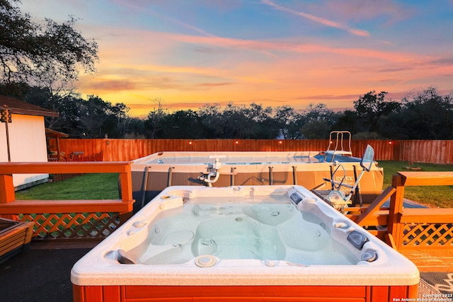 deck at dusk featuring a hot tub and a yard