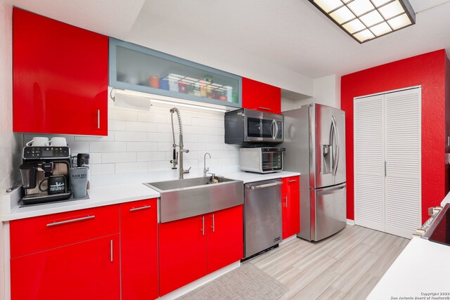 kitchen with backsplash, sink, appliances with stainless steel finishes, and light wood-type flooring