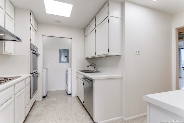 kitchen with a skylight, white cabinets, wall chimney exhaust hood, sink, and light tile flooring