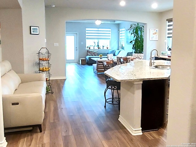 kitchen featuring a breakfast bar, a center island with sink, sink, dark hardwood / wood-style flooring, and light stone counters