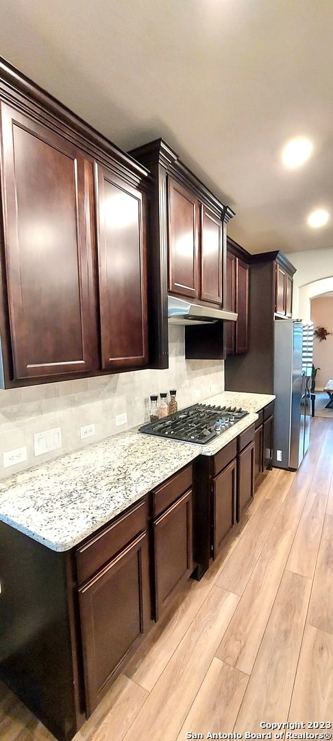 kitchen featuring light stone countertops, tasteful backsplash, stainless steel appliances, and light hardwood / wood-style flooring