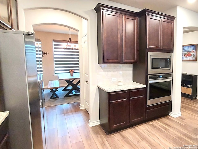 kitchen featuring backsplash, light hardwood / wood-style floors, a notable chandelier, and appliances with stainless steel finishes