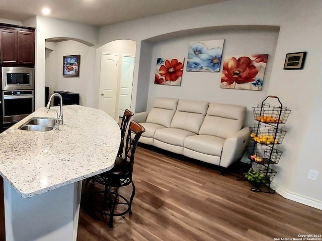 kitchen with dark hardwood / wood-style floors, appliances with stainless steel finishes, sink, light stone counters, and dark brown cabinetry