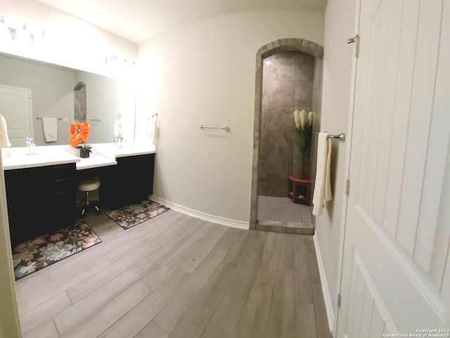 bathroom with a tile shower, double sink vanity, and hardwood / wood-style flooring