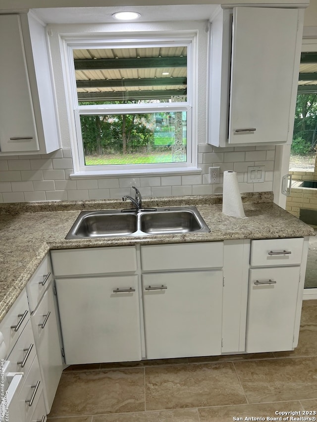 kitchen featuring light tile flooring, tasteful backsplash, sink, light stone countertops, and white cabinets