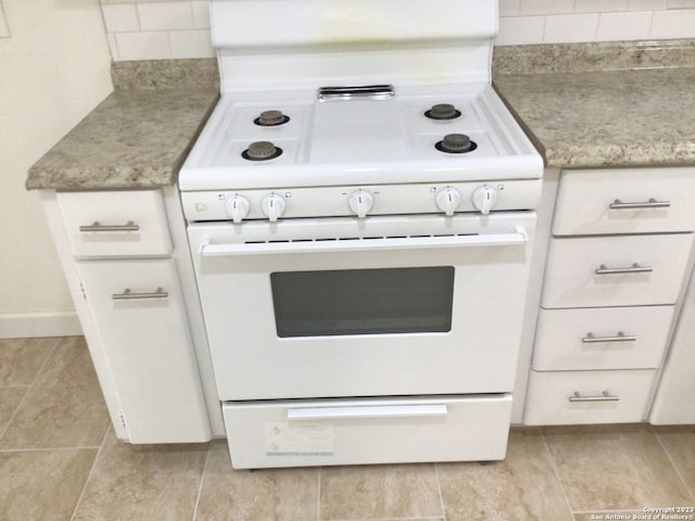 kitchen with light tile flooring, tasteful backsplash, light stone counters, white stove, and white cabinets