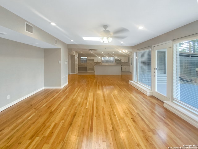 unfurnished living room featuring ceiling fan, a skylight, and light hardwood / wood-style flooring