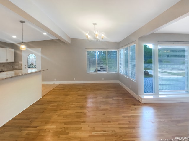 unfurnished dining area with lofted ceiling with beams, a chandelier, and light wood-type flooring