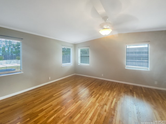 empty room with ceiling fan, vaulted ceiling, crown molding, and light hardwood / wood-style flooring